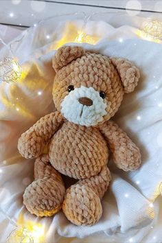 a brown teddy bear sitting on top of a white cloth covered pillow with lights in the background