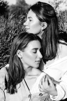 two beautiful young women standing next to each other in front of some grass and flowers