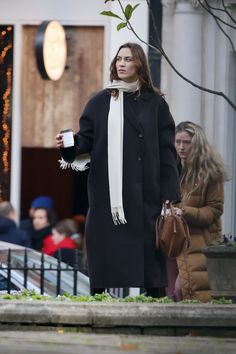 a woman is walking down the street with her coffee in hand and wearing a scarf around her neck