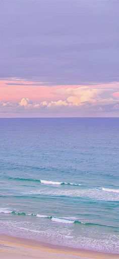 two people walking on the beach carrying surfboards under an overcast sky at sunset