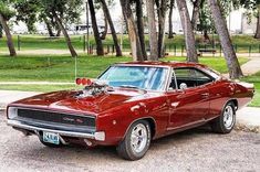 a red muscle car parked in front of some trees