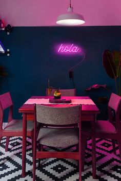 a pink neon sign above a table with chairs