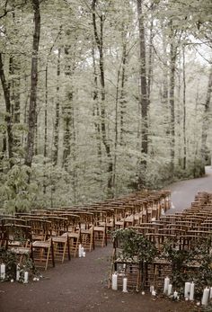 rows of wooden chairs set up for an outdoor ceremony in the woods with candles on them