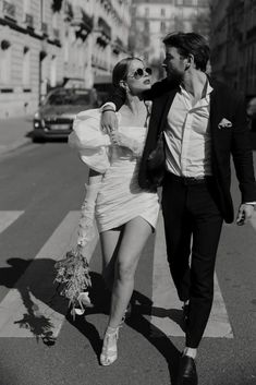 a man and woman walking across a cross walk in the street together, dressed in white