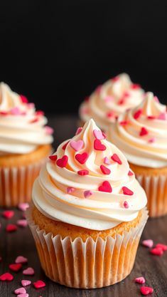 three cupcakes with white frosting and pink sprinkles