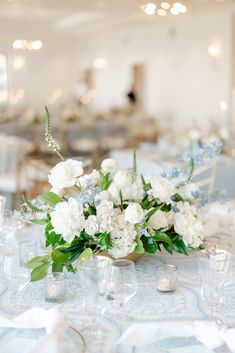 white flowers and greenery are on the centerpieces of this table at a wedding reception