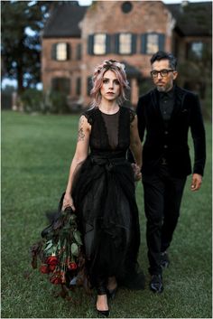 a man and woman walking in front of a large house with flowers on the grass