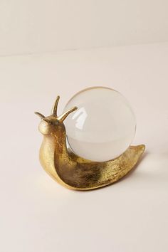 a glass ball sitting on top of a golden banana shaped figurine with an egg in the shape of a snail