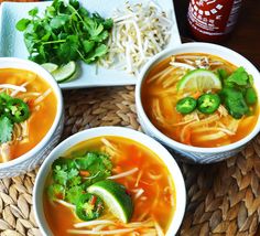 three bowls of soup with limes, cilantro and shredded cheese on the side