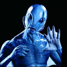 an alien man with blue paint on his face and hands, holding something in one hand