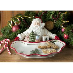 a santa clause sitting in a bowl with cookies and candy canes on the table