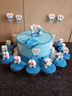 a cake with blue frosting and white elephants on top is surrounded by cupcakes