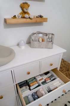 an open drawer in a white dresser next to a teddy bear on top of a shelf