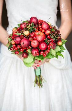 a bride holding a bouquet of apples and berries