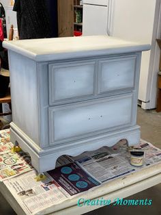 an old dresser is being painted white with blue paint and newspaper on the floor next to it