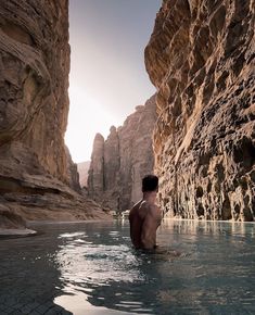 a man sitting in the middle of a river next to some rocks and water with his back turned towards the camera