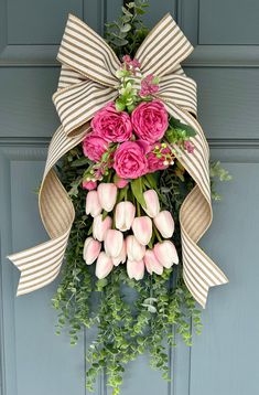 a bouquet of pink flowers is hanging on the front door with a bow around it