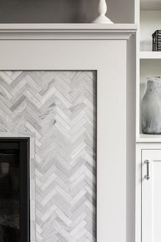 a fireplace with white and grey herringbone tile on the mantel in a living room