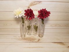 three clear vases with red and white flowers in them on a wooden wall background