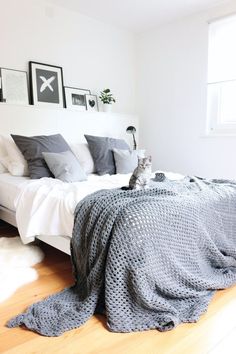 a cat sitting on the edge of a bed next to pillows and blankets in a bedroom