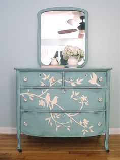 a blue dresser with white flowers painted on it and a mirror over the top of it