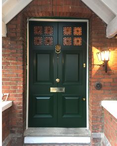 a green front door on a brick building with two lights above it and below the door is a window