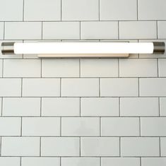 a bathroom light mounted on the side of a white brick wall