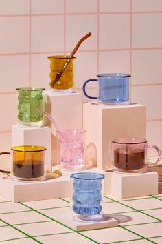 four different colored cups are stacked on top of each other in front of a pink tiled wall