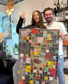 two people standing next to each other holding up a piece of art