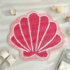 a bath mat with a pink shell on it next to slippers and seashells