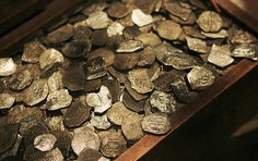 a pile of silver coins sitting on top of a wooden table next to an open suitcase