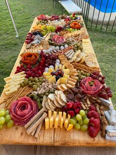 a wooden table topped with lots of different types of cheese and crackers next to a swimming pool