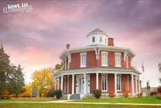 an old red brick house with white trim and columns on the front porch is shown at sunset