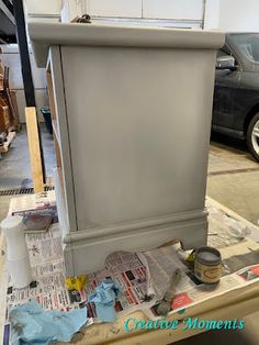 a gray cabinet sitting on top of a wooden table next to a black car in a garage