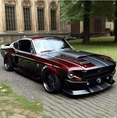 a red and black mustang parked on the side of a road in front of a building