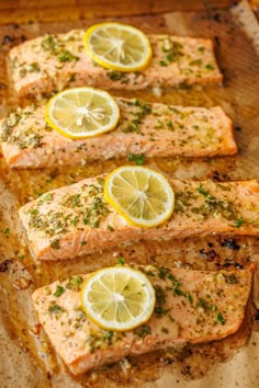 four pieces of salmon with lemons and parsley on top, sitting on a baking sheet