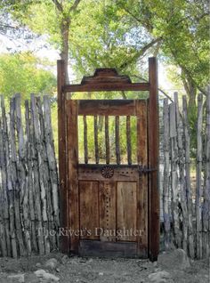 an old wooden gate in front of a wood fence with a tree on the other side