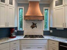 a kitchen with white cabinets and a copper hood over the stove, along with marble counter tops