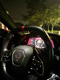 the interior of a car with dashboard lights and steering wheel controls at night, in front of trees