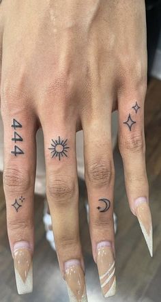 a woman's hand with tattoos on it and two fingers that have arrows, stars, and the moon