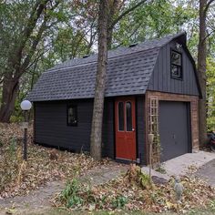 a small black shed with a red door in the middle of some trees and leaves