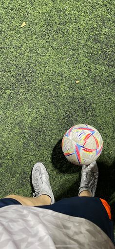 a person is sitting on the grass with a soccer ball in their hand and his feet propped up