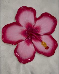 a pink flower sitting on top of a white sheet with a yellow bead in the middle