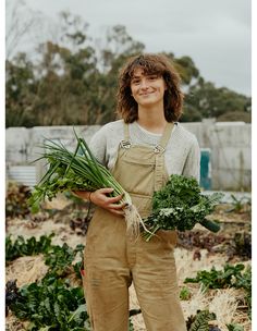 a woman in overalls holding some vegetables