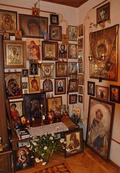 a room filled with pictures and paintings on the wall next to a wooden table topped with flowers