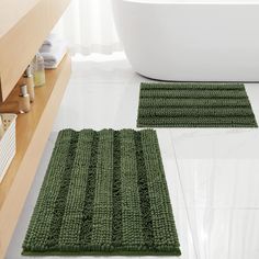 two green bath mats sitting on top of a white floor next to a tub in a bathroom