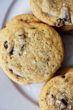 four cookies sitting on top of a white plate covered in chocolate chips and sea salt