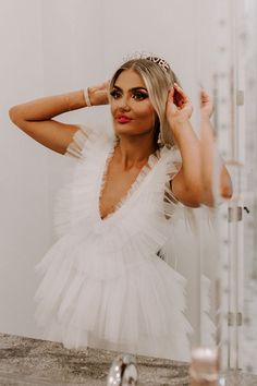 a woman in a white dress is looking at herself in the mirror and holding her hair