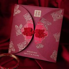 a wedding card with red flowers on it next to a gold bangle bracelet and ring