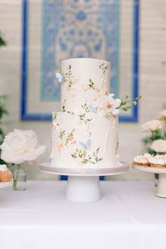 a white cake with flowers on it sitting on a table next to cupcakes